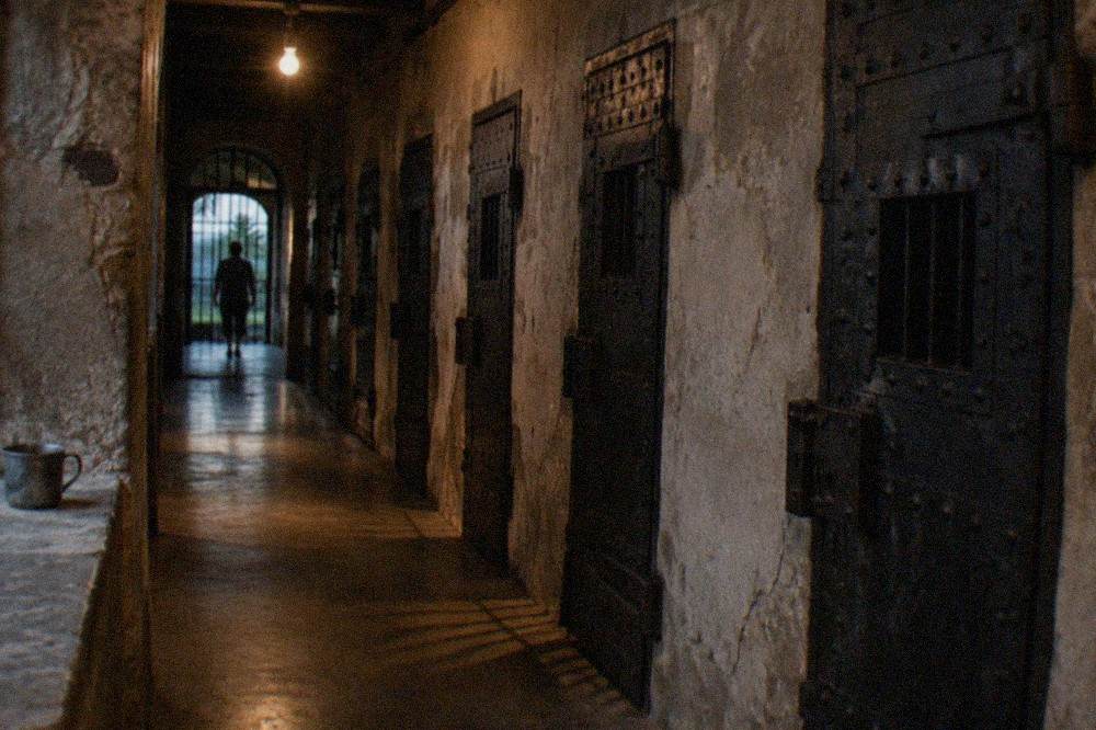 A dimly lit jail corridor with iron cell doors along one side