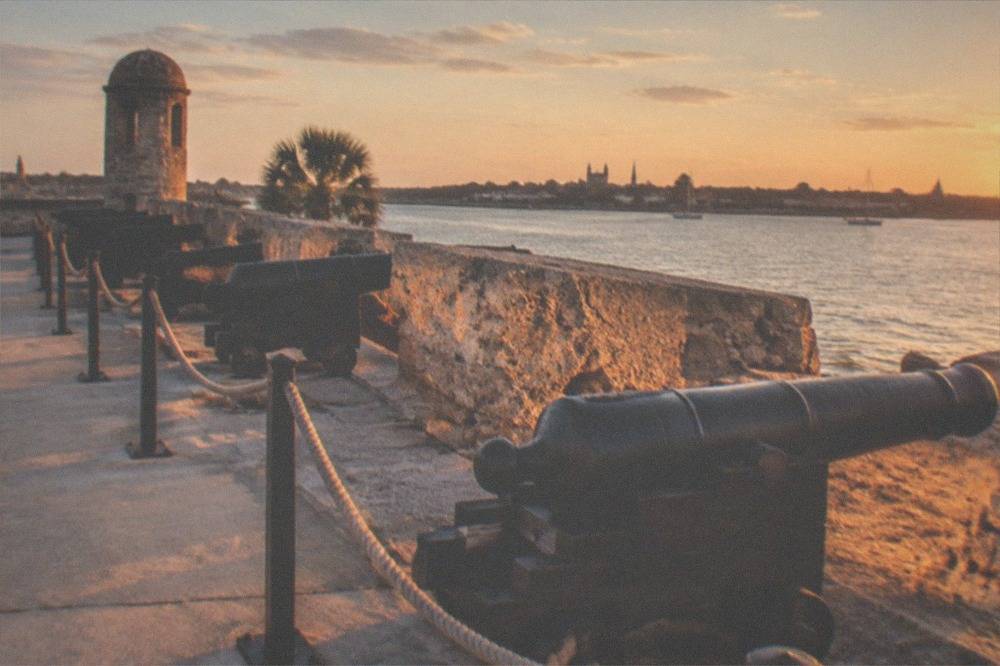 Ancient coquina stone fortress walls and cannon rows beside a river at dusk