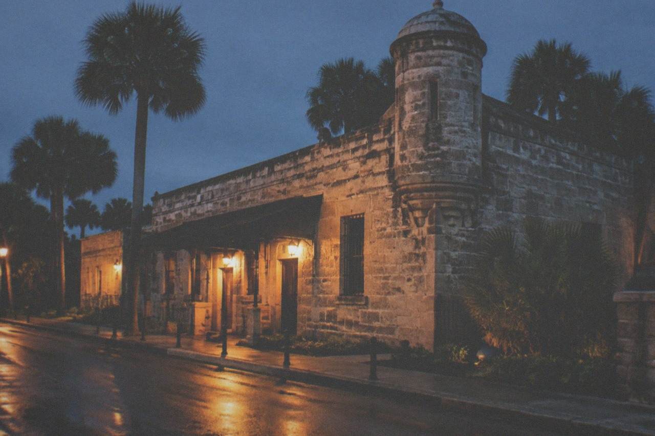 The stone walls and tower of the old county jail lit by evening lamps along a quiet St. Augustine street