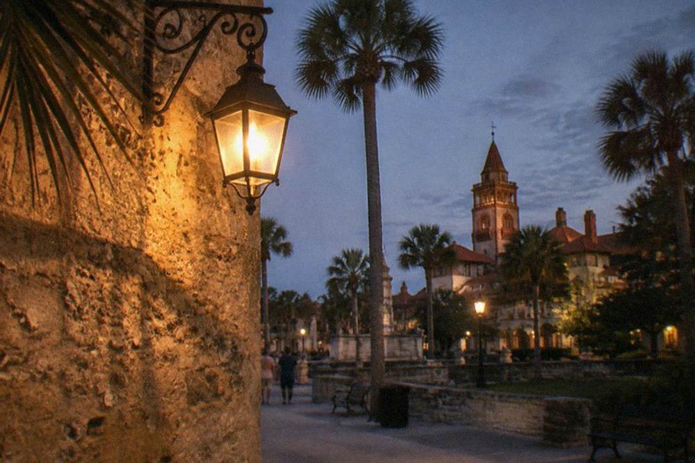A lit lantern hanging beside a centuries-old coquina wall at night
