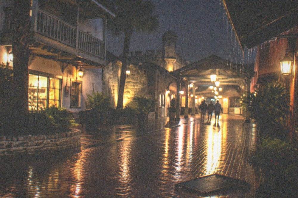 Rain-slicked brick street reflecting lantern light at night