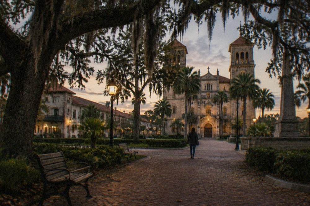 Live oak trees draped with Spanish moss in a lamplit historic plaza at dusk