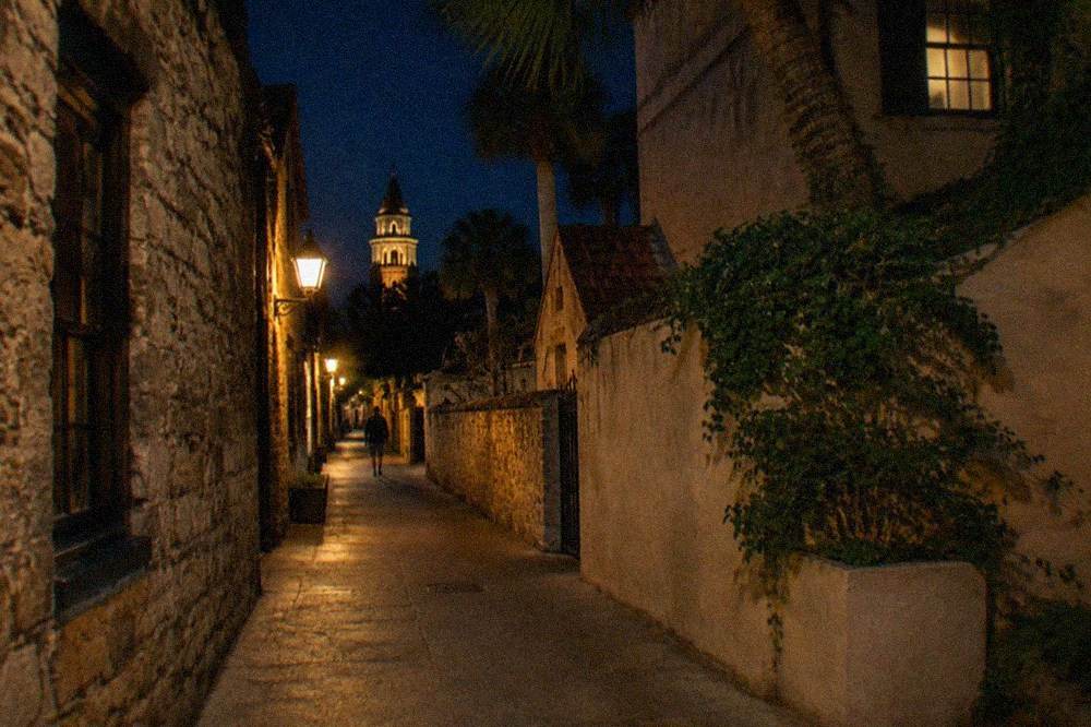A narrow pedestrian lane of historic coquina buildings lit by warm street lamps at night