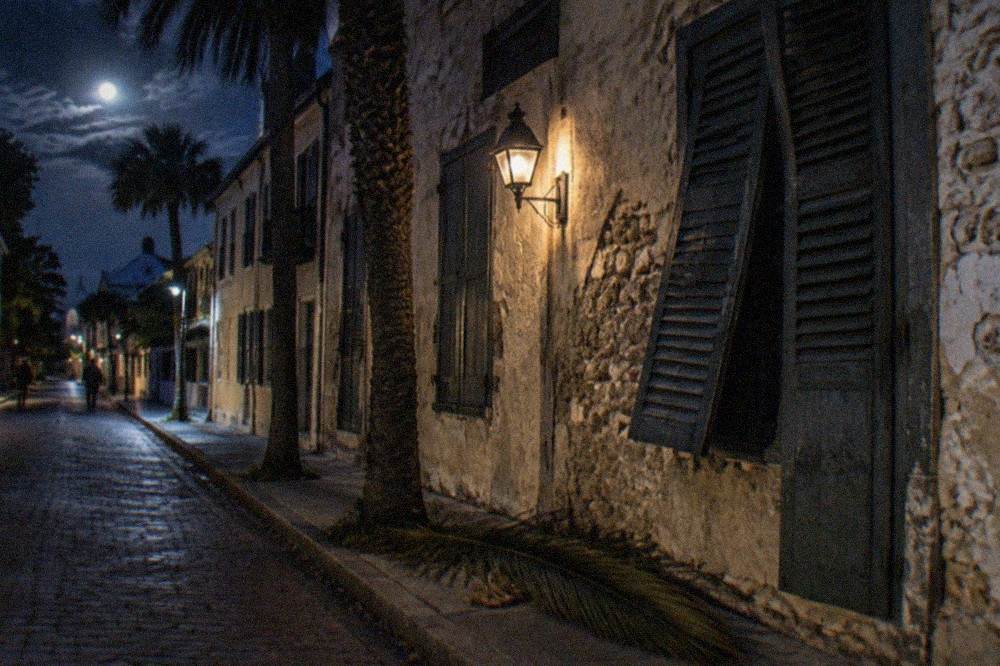 A darkened historic street with a lantern glowing outside closed storefronts at night