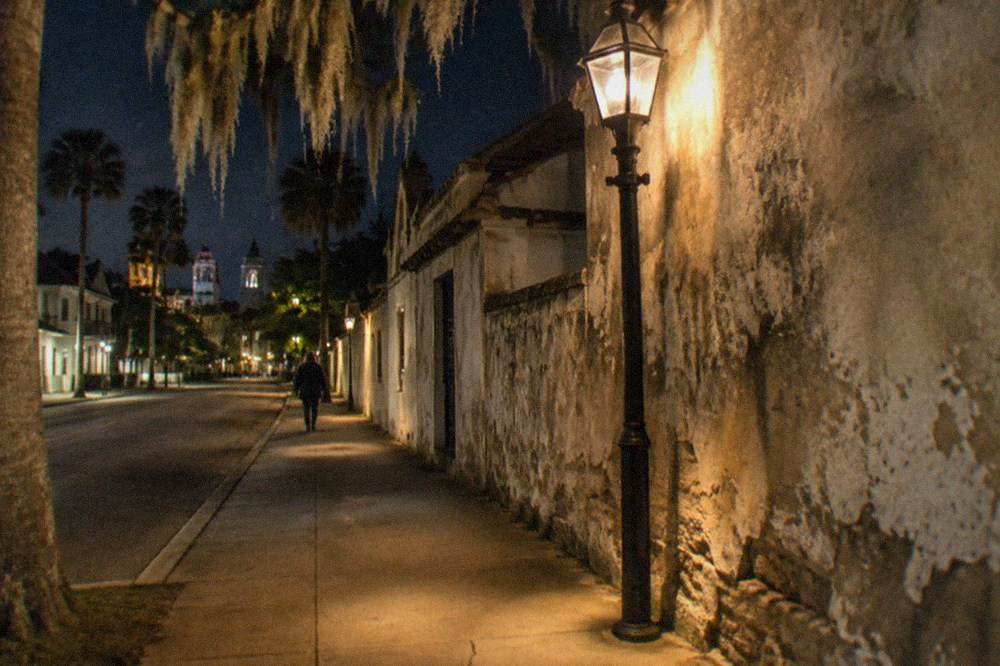 Historic buildings along a nighttime street lit by warm lamps above an empty sidewalk