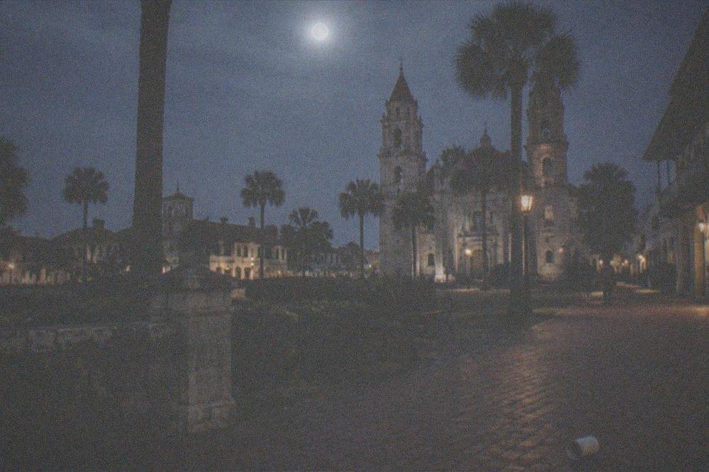 A moonlit plaza with historic stone buildings and palm silhouettes