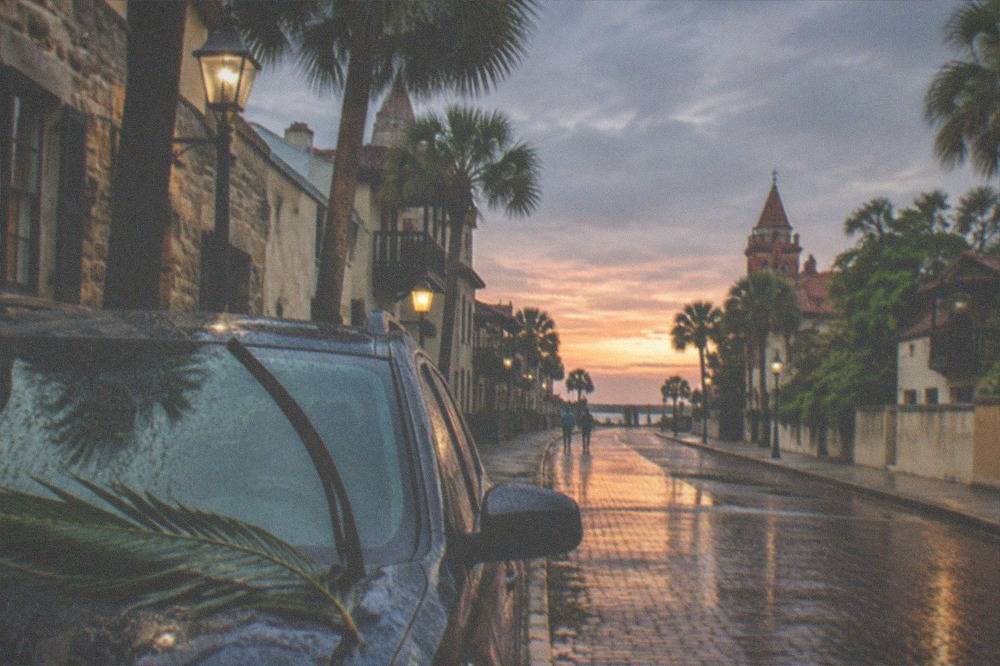 A cobblestone street at dusk with parked cars and old stone buildings