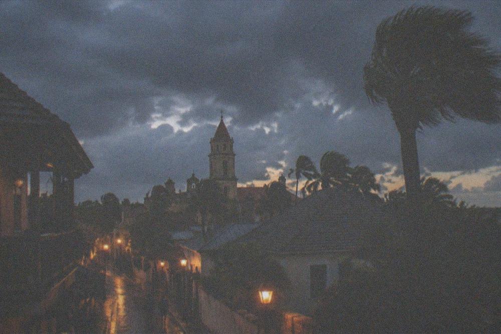 A dusk sky over the rooftops and old tower of a historic district with warm streetlight beginning to glow