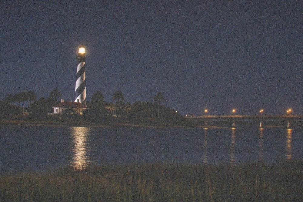 The illuminated lighthouse tower against a starry night sky over the island