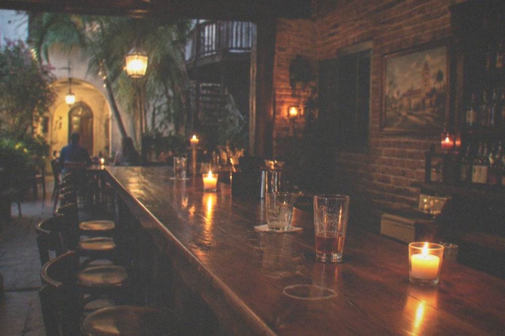 A candlelit tavern interior with a long wooden bar and empty stools
